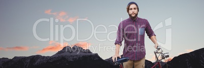 Millennial man with bicycle against mountain tops and evening sky