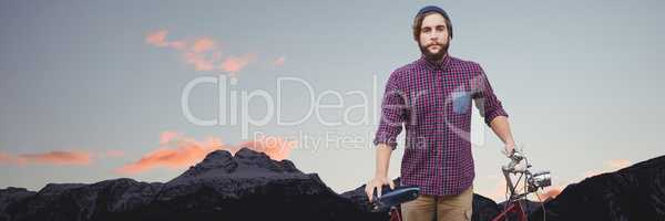 Millennial man with bicycle against mountain tops and evening sky