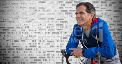 Middle aged man on bicycle against grey brick wall