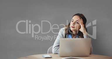 Worried business woman at a desk using a computer against grey background