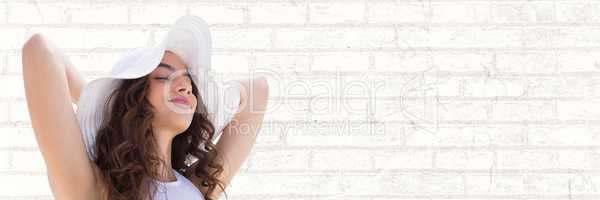 Portraiture of woman in summer hat relaxing against white brick wall