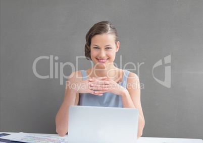 Happy business woman at a desk  using a computer against grey background
