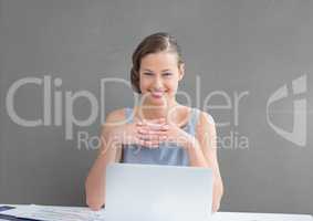 Happy business woman at a desk  using a computer against grey background