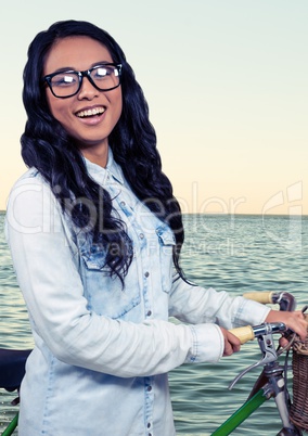 Millennial woman with bicycle against water