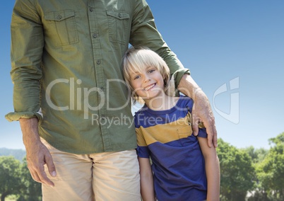 Father arm around son against sky and blurry trees