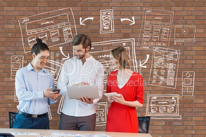 Happy business people at a desk looking at computer and tablets against brick wall with graphics