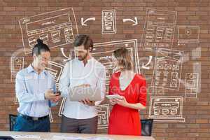 Happy business people at a desk looking at computer and tablets against brick wall with graphics