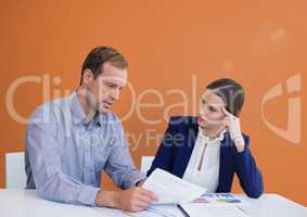 Business people at a desk looking at a paper against orange background