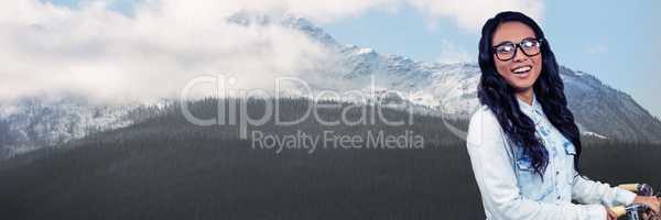 Millennial woman on bicycle against snowy mountain with trees