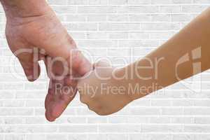 Close up of father and son holding hands against white brick wall