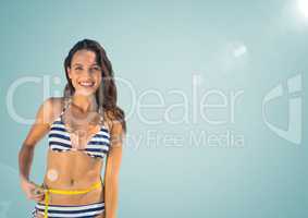 Millennial woman in bikini with measuring tape against light blue background with flare