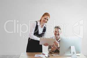 Happy business people at a desk using a tablet against white wall