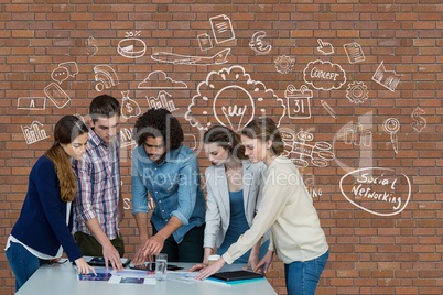 Business people at a desk pointing a tablet against brick wall with graphics