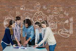 Business people at a desk pointing a tablet against brick wall with graphics