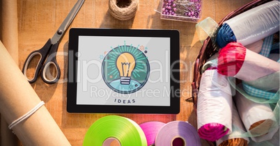 Tablet displaying ideas light bulb on table with sewing materials