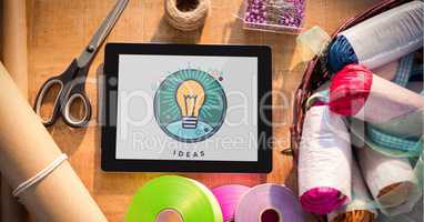 Tablet displaying ideas light bulb on table with sewing materials