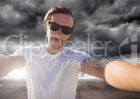 man taking casual selfie photo in front of dramatic dark cloud landscape