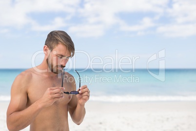 Man at the beach holding sunglasses