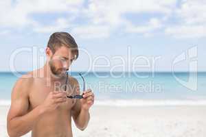 Man at the beach holding sunglasses