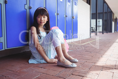 Portrait of schoolgirl sitting on pavement by lockers