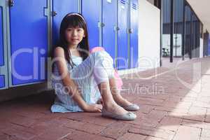 Portrait of schoolgirl sitting on pavement by lockers