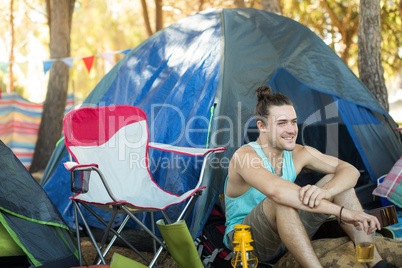 Thoughtful man holding beer glass while sitting at campsite