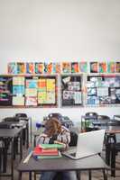 Tired schoolboy sleeping on stack of book sitting in classroom