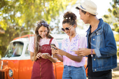 Smiling friends using phone while standing on field