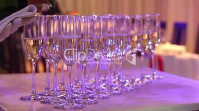 The waiter pours champagne in wineglass, in a restaurant, The waiter pours champagne in crystal glasses, Restaurant interior, buffet table, Waiter in white gloves, close-up