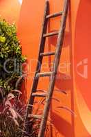 Rustic wooden ladder against a bright orange wall