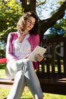 Woman sitting on bench and using digital tablet in garden