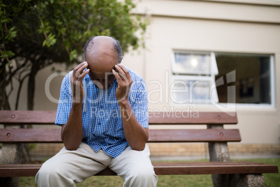 Upset senior man sitting with head in hands on bench