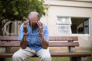 Upset senior man sitting with head in hands on bench