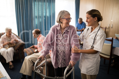 Smiling female doctor looking at senior woman standing with walker