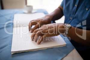 Midsection of senior man reading braille book at table