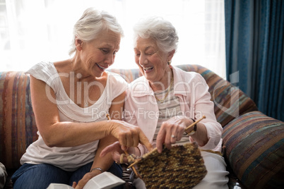 Cheerful senior women talking about knitting while sitting on sofa against window