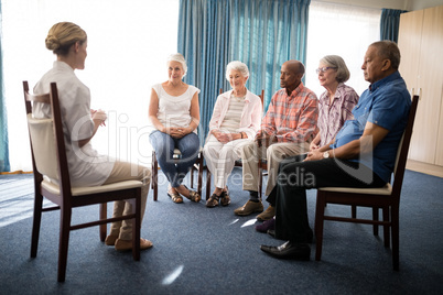 Female doctor sitting with senior people on chairs against window