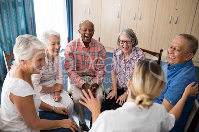 Cheerful seniors sitting with female doctor on chairs