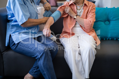 Low section of doctor checking senior woman blood pressure