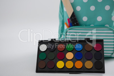 Schoolbag with various supplies and palette on white background