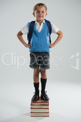 Schoolboy standing on books stack against white background