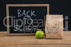 Lunch paper bag, green apple and slate with text back to school on wooden table