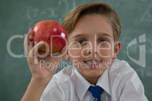 Schoolboy holding red apple against chalkboard