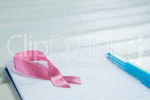 High angle view of pink Breast Cancer Awareness ribbon and spiral notepad with pen