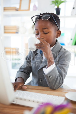 Boy imitating as businessman having coffee while using computer at desk
