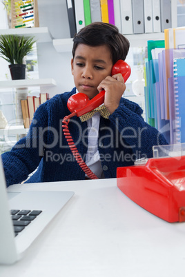 Businessman using laptop while talking on landline phone