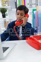 Businessman using laptop while talking on landline phone