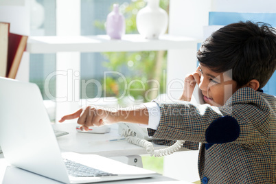 Profile view of businessman using telephone while pointing on laptop