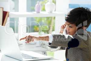 Profile view of businessman using telephone while pointing on laptop