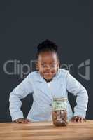Portrait of smiling woman with coins in glass jar against gray wall